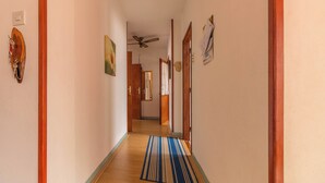 Un couloir avec un plancher en bois, un tapis à rayures, un ventilateur de plafond et une porte dotée d’un miroir.