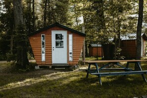 A small wooden cabin with a white door, surrounded by trees.