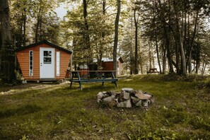A rustic cabin with a wooden exterior, a small porch, and a picnic table in a forested area.