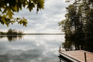 A calm lake with a wooden dock extending into the water, surrounded by dense trees.