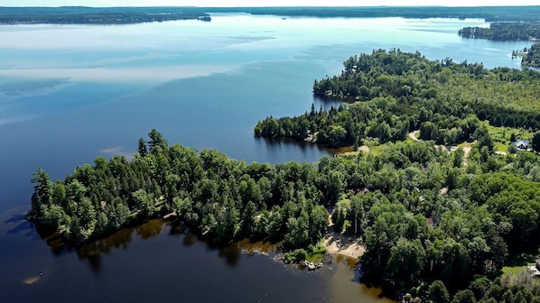 An aerial view of a forested island with a lake, surrounded by dense trees and a few buildings.