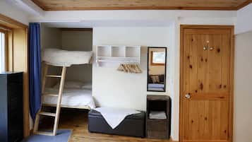A compact room with a bunk bed, a desk, a wardrobe, and a door.