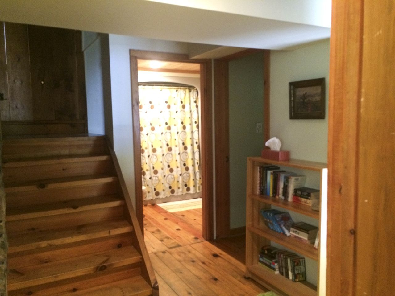A wooden staircase leading to a room with a bookshelf and a door with a curtain.