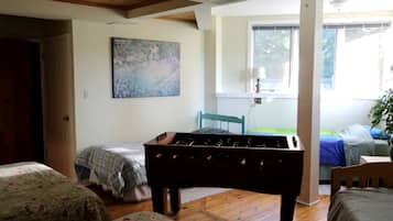 A room with a wooden floor, a bed with a floral bedspread, a sofa with a floral cover, a painting on the wall, and a window with blinds.