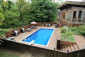 A backyard with a swimming pool, deck furniture, and a wooden deck.