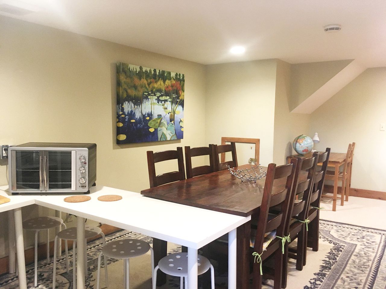 A dining area with a wooden table, chairs, a microwave, and a painting on the wall.