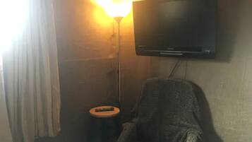 A room with a television mounted on the wall, a small round stool, and a chair.