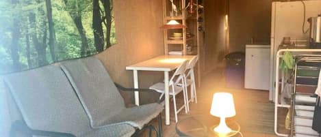 Una habitación con sofá, una mesita, lámpara, refrigerador y una pared con un mural de un bosque.