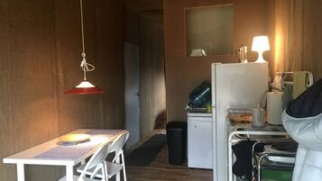A compact kitchen with a refrigerator, a sink, a table with chairs, and a hanging light fixture.