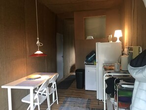 A compact kitchen with a refrigerator, a sink, a table with chairs, and a hanging light fixture.