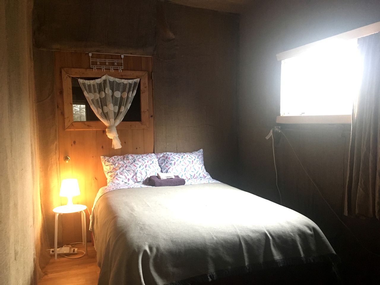 A single bed with a headboard, a bedside lamp, and a window with curtains.