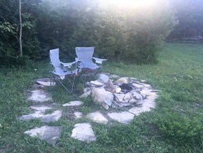 A fire pit with rocks and two folding chairs in a grassy outdoor area.