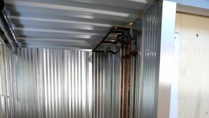 A metal-walled room with a wooden floor, a vertical metal pipe, and a wooden door. - Tiny House Rental in Markdale Perfect for a Couple's Retreat in Ontario (Markdale)