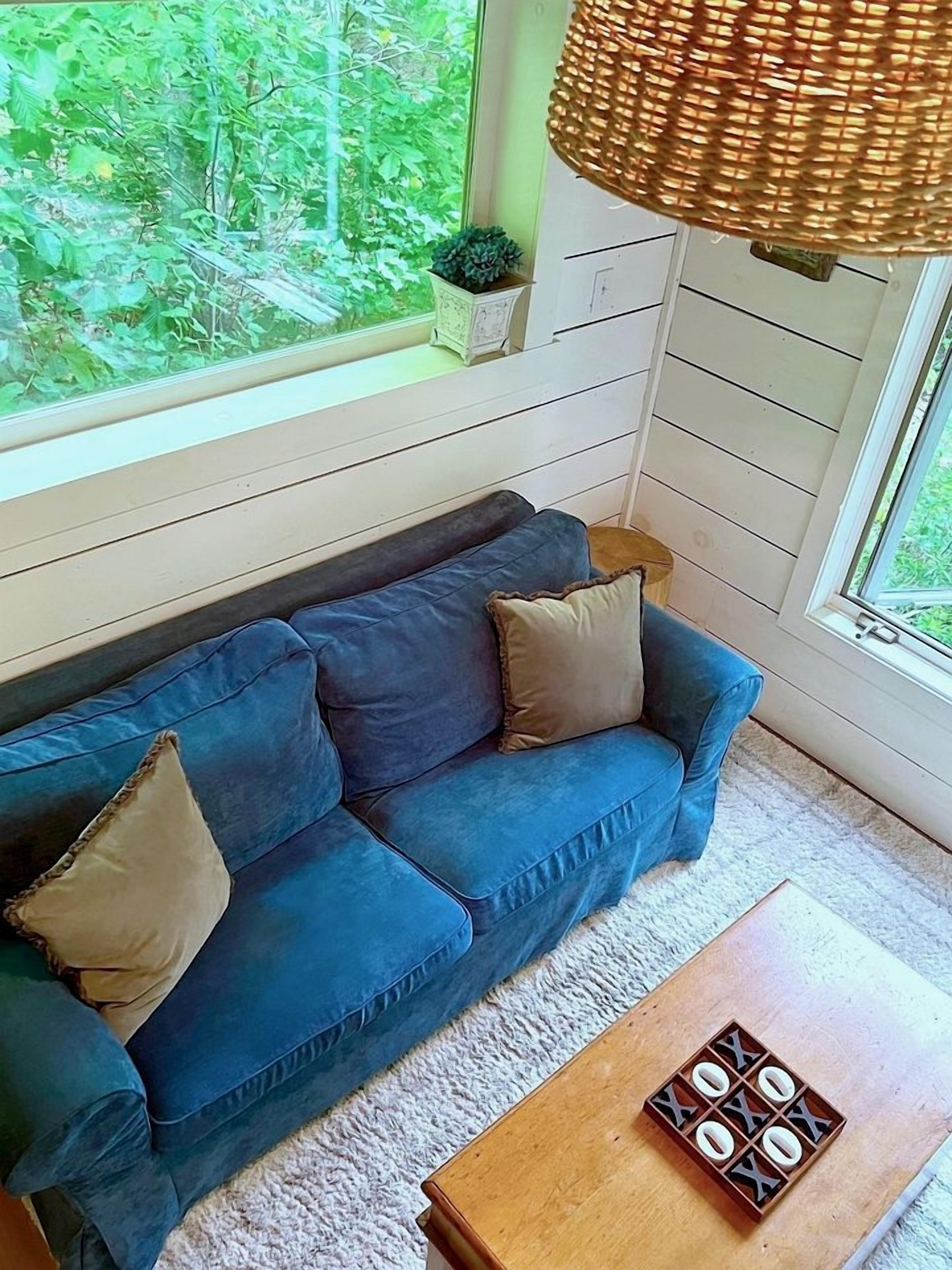 Ein blaues Sofa mit Kissen, ein Holztisch mit einem Spielzeug und Blick auf Grün durch ein Fenster.