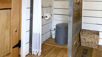 Une porte en bois, un rideau blanc, une poubelle grise et un tapis tissé sur un plancher en bois.