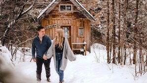 Eine Holzhütte mit der Aufschrift 'The Cabin', verbunden durch einen verschneiten Pfad, umgeben von kahlen Bäumen.
