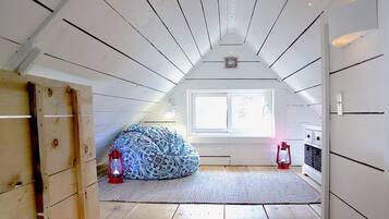 A room with a sloped ceiling, a window, a bed with patterned bedding, and two lanterns.