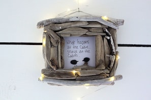 Decoración rústica con temática de cabaña, un mensaje y elementos naturales, rodeada de luces colgantes.