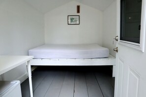 A small, white room with a single bed, a small table, a window, and a door.