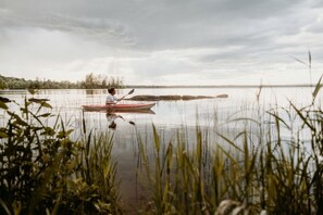 A calm lake with a kayak and a person paddling, surrounded by tall grasses and trees in the background.