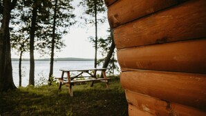 Una cabaña de madera con una mesa de picnic y vista a un lago.