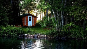 Una cabaña junto a un lago, rodeada de árboles.