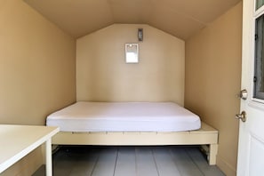 A small, single-bed room with a white mattress, a small table, and a door with a window.