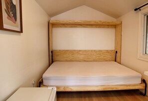 A single bed with a wooden frame and mattress in a room with a sloped ceiling and a window.