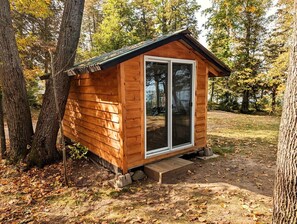 A small wooden cabin with a glass door, surrounded by trees and a dirt path. - Golden Lake Glamping Cabin for an Outdoor Adventure in Killaloe, Ontario (Killaloe)