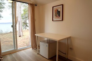 A room with a desk, a small refrigerator, a window with curtains, and a framed picture on the wall.