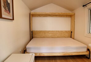Un lit simple avec un cadre en bois, dans une pièce dotée d’un plafond en pente et d’une fenêtre.