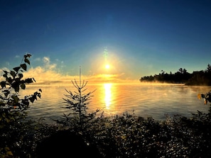 A sunrise over a calm lake with trees in the foreground. - Golden Lake Glamping Cabin for an Outdoor Adventure in Killaloe, Ontario (Killaloe)