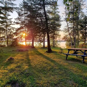 Ein Picknicktisch in einer grünen Wiese, im Hintergrund Bäume und ein Gewässer.