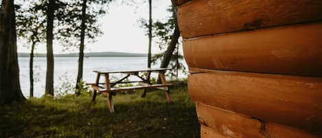 A wooden cabin with a picnic table and a view of a lake.