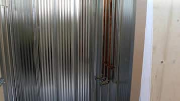 Une pièce aux murs métalliques, dotée d’un plancher en bois, d’un tuyau métallique vertical et d’une porte en bois.