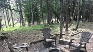 A forest setting with three Adirondack chairs arranged around a campfire. - Rural Cabin Surrounded by Beautiful Nature in Ontario (Markdale)