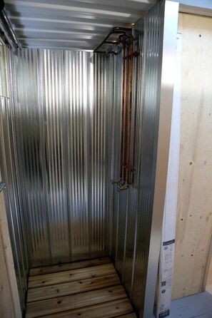 Una habitación con paredes de metal, suelo de madera, una tubería metálica vertical y una puerta de madera.