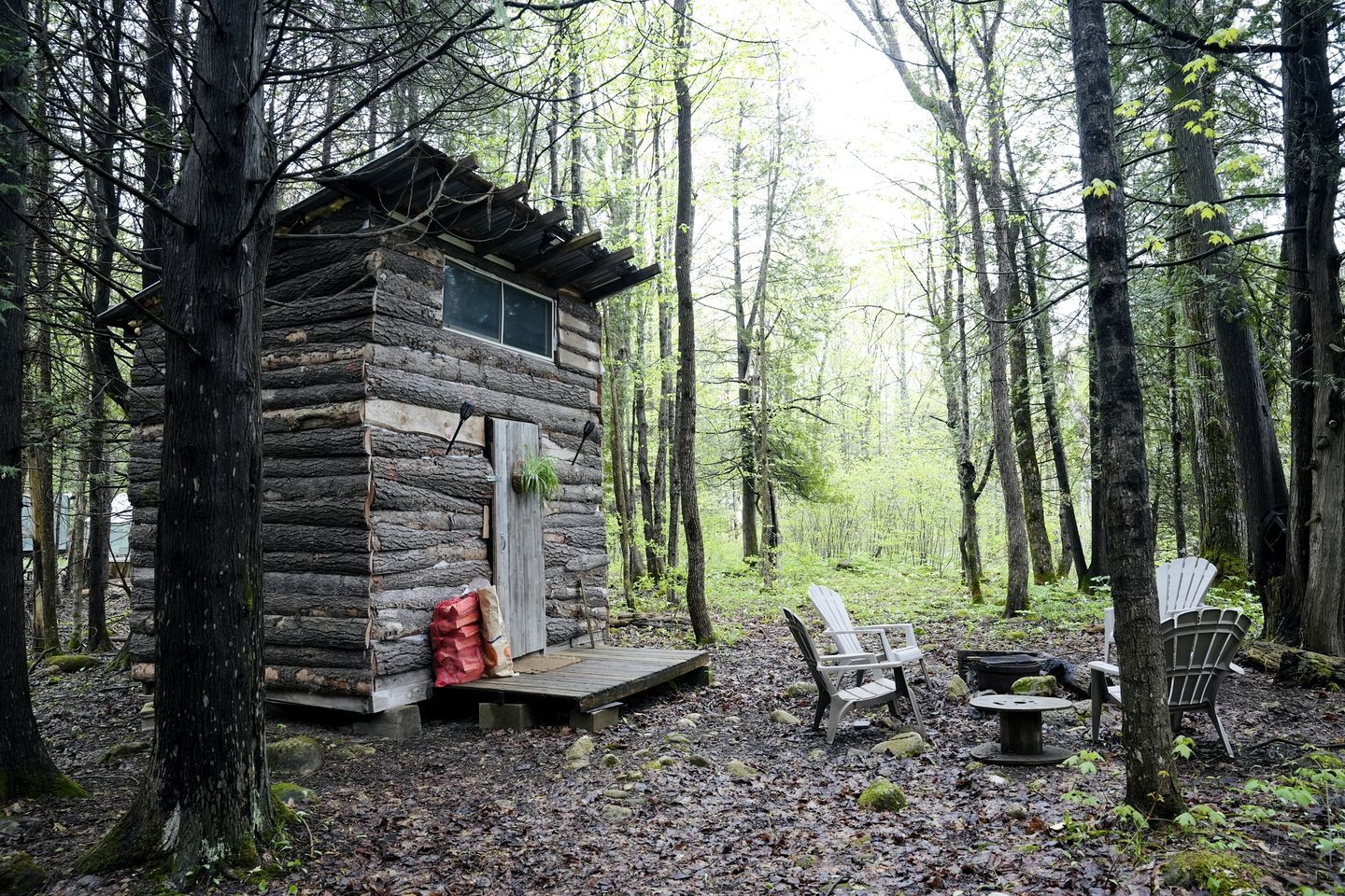 A rustic cabin with a wooden deck, surrounded by a forest.