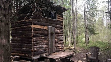 Una cabana rústica de fusta amb un balcó de fusta i una única porta, envoltada per un bosc.
