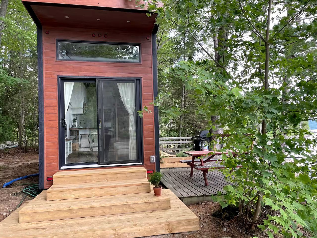 A modern cabin with a wooden deck, a glass door entrance, and a small outdoor table.