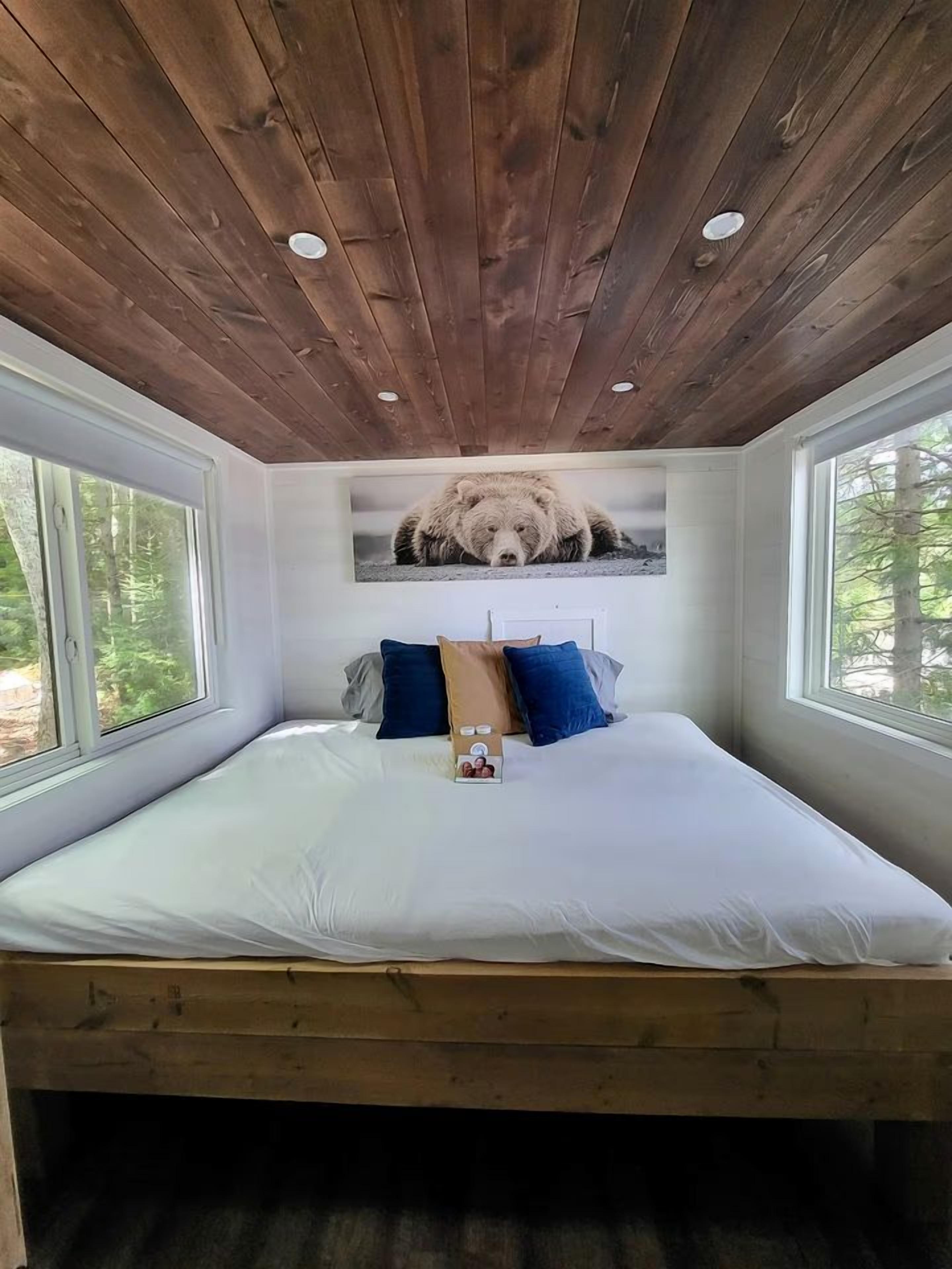 A bedroom with a wooden ceiling, a large bed with white bedding, and a bear picture on the wall.