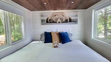 A bedroom with a wooden ceiling, a large bed with white bedding, and a bear picture on the wall.