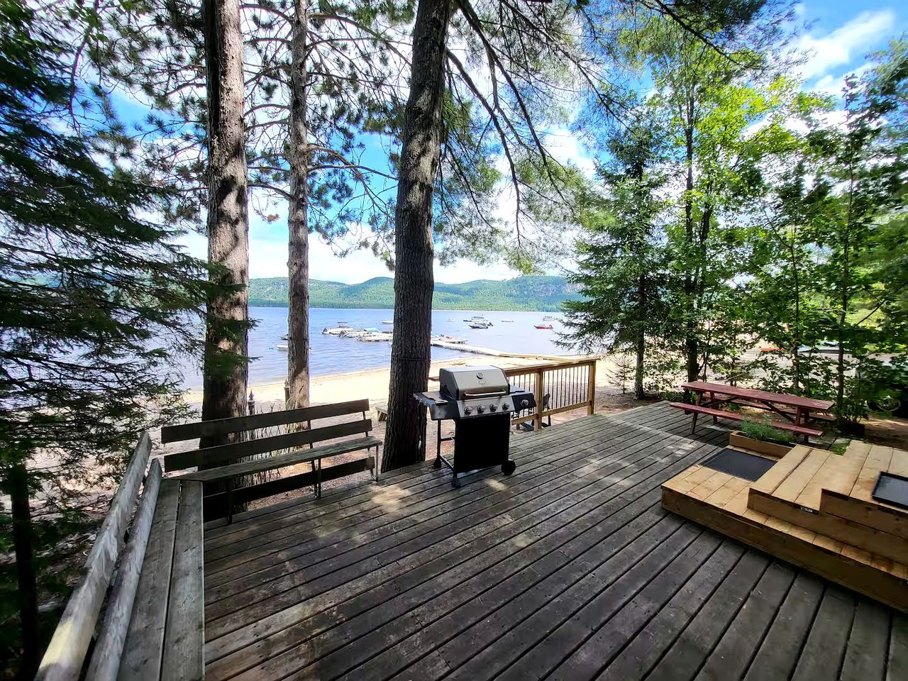 A wooden deck with a grill, benches, and a view of a lake.