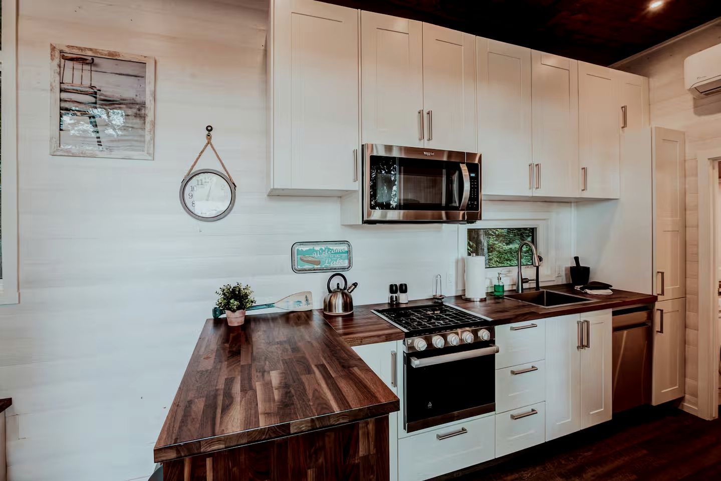 Une cuisine avec des meubles blancs, un four à micro-ondes en acier inoxydable, une cuisinière à gaz et un plan de travail en bois.