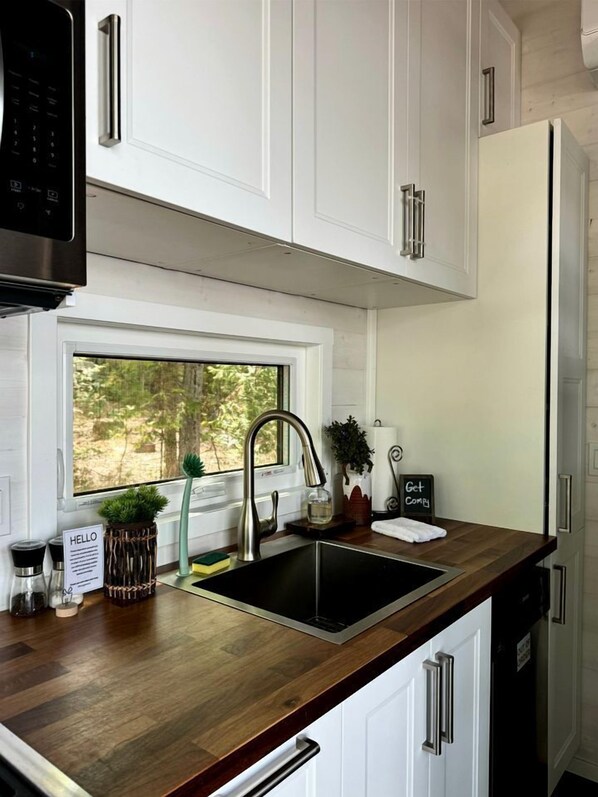 A modern kitchen with white cabinets, a stainless steel sink, and a window overlooking greenery.