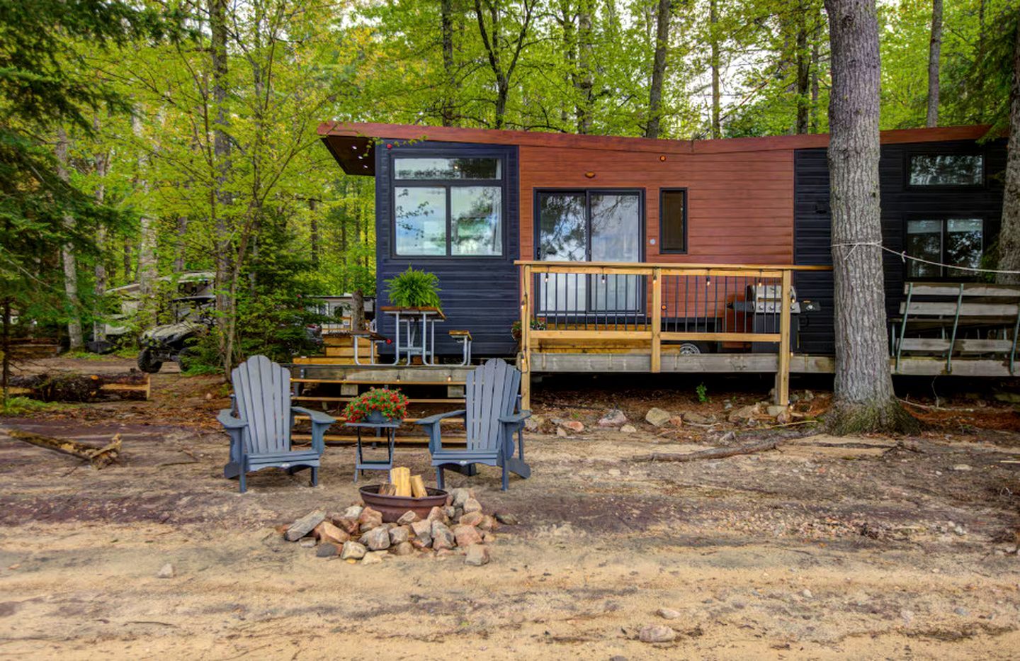 Une cabane dotée d’une terrasse, de deux fauteuils Adirondack, d’un foyer et entourée d’une forêt.
