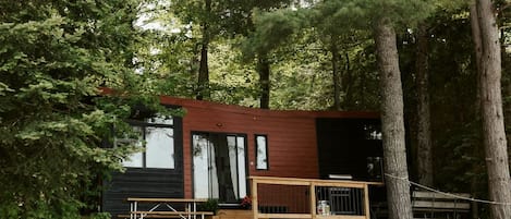 A cabin with a deck, two Adirondack chairs, and a wooden staircase leading to the entrance.