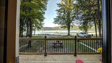 A deck with a view of a lake, trees, and a parked vehicle.
