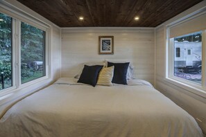 Ein Schlafzimmer mit Holzboden, einem Bett mit weißer Bettwäsche und zwei Fenstern.