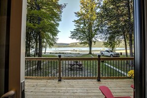 A deck with a view of a lake, trees, and a parked vehicle.
